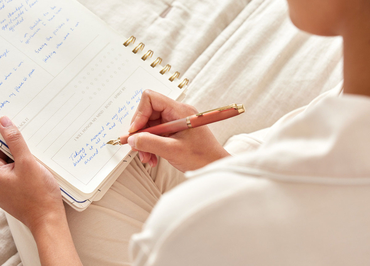 Osoba pisząca w notesie piórem wiecznym Parker IM Rituals Uplifting Orange GT [2203900] w ciepłym odcieniu pomarańczu ze złotymi wykończeniami.